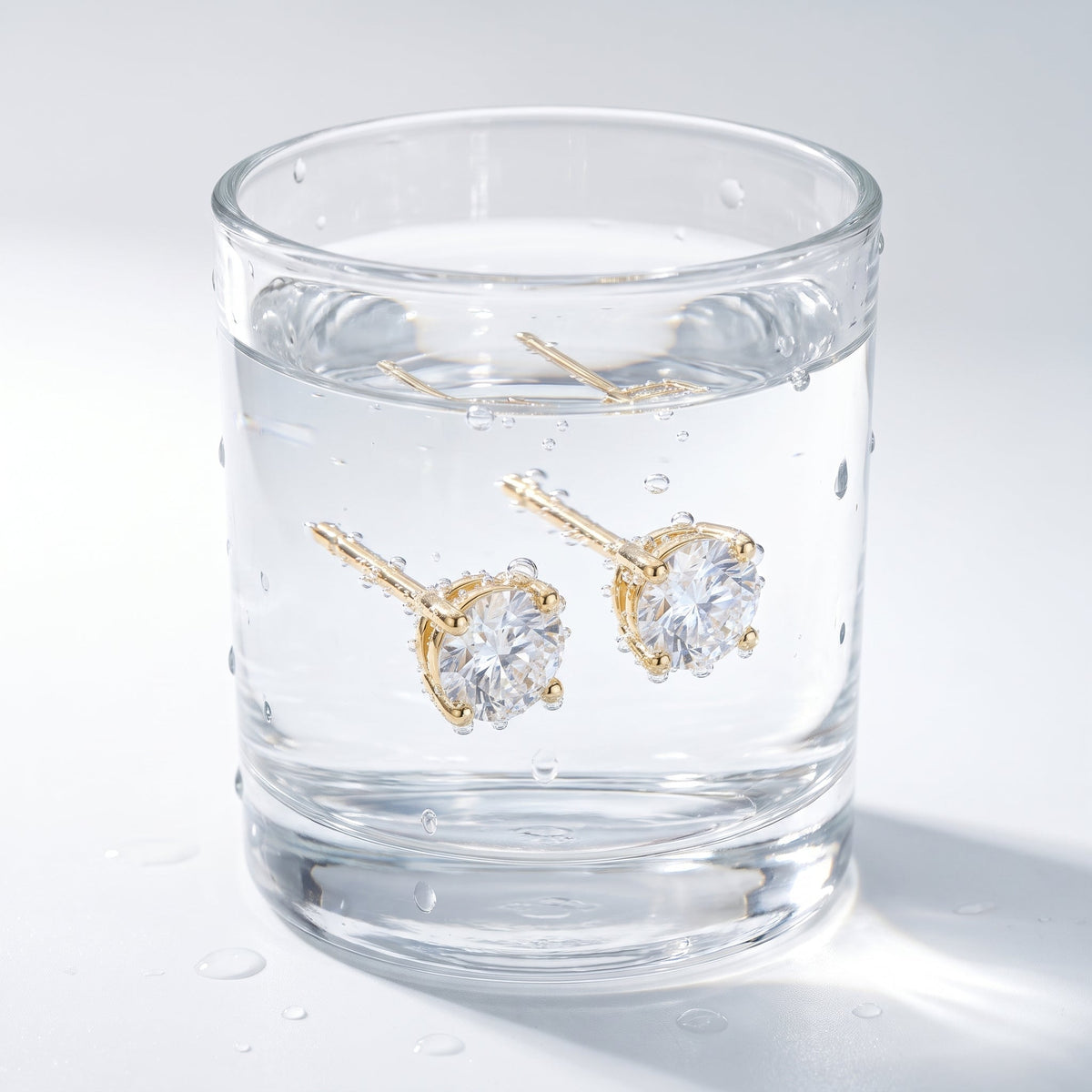 Pendientes punto de luz con circonita bañados en oro de 18K en un vaso de agua