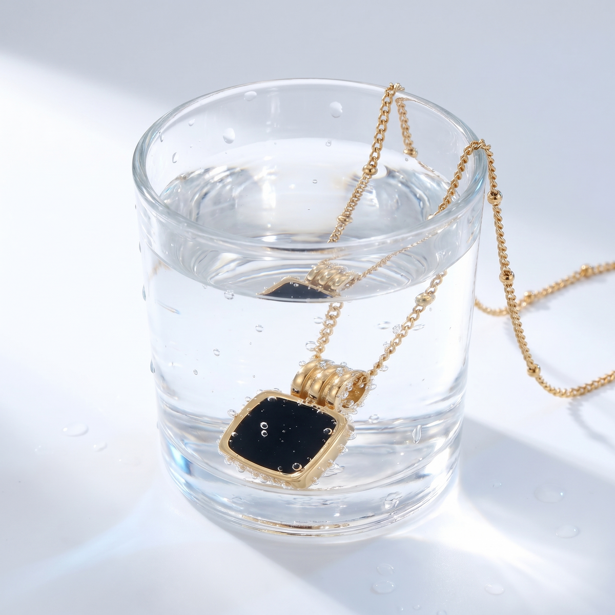 Collar con colgante de concha negra bañado en oro de 18K en un vaso de agua