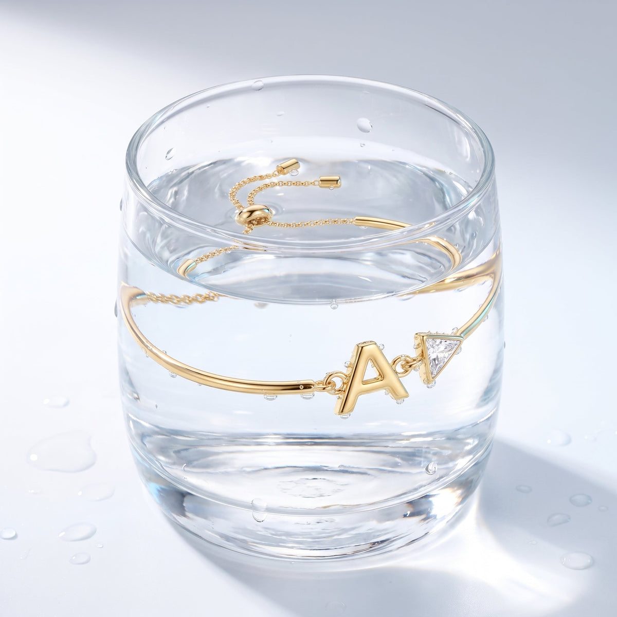 Pulsera con inicial y cristal bañada en oro de 18K en un vaso de agua