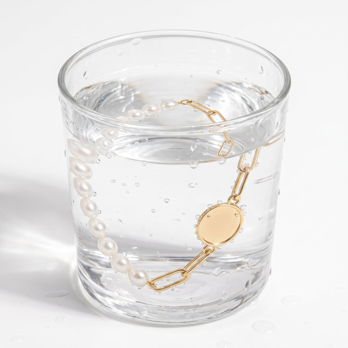 Pulsera de perlas y paperclip bañada en oro de 18K en un vaso de agua