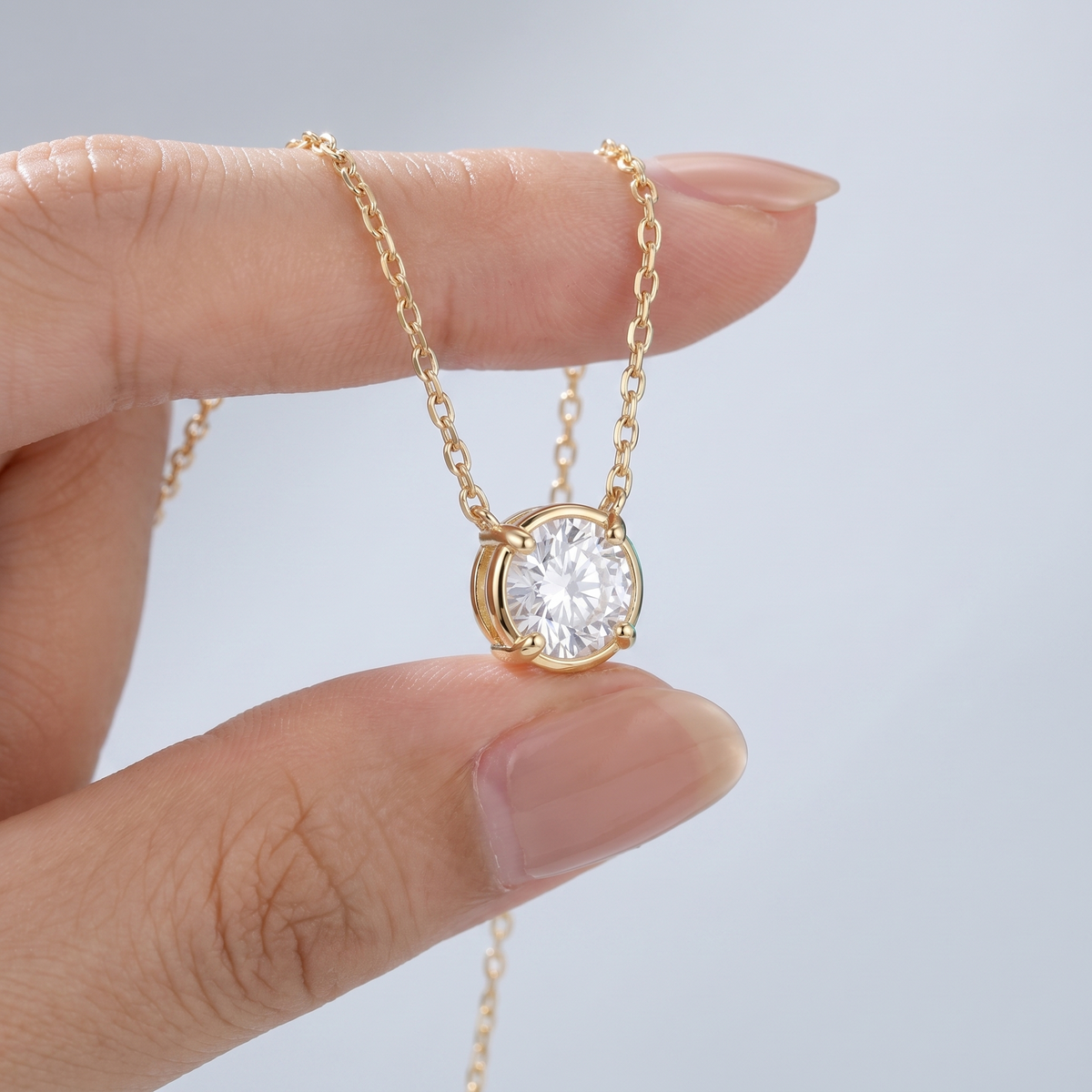 Collar punto de luz mini con circonita bañado en oro de 18K sostenido entre los dedos, para ver el tamaño real
