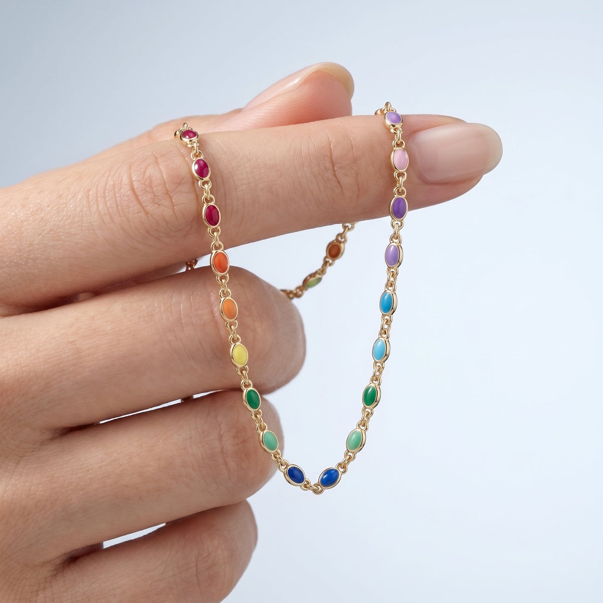 Gargantilla arcoíris de piedras de colores bañada en oro de 18K sostenida entre los dedos, para ver el tamaño real