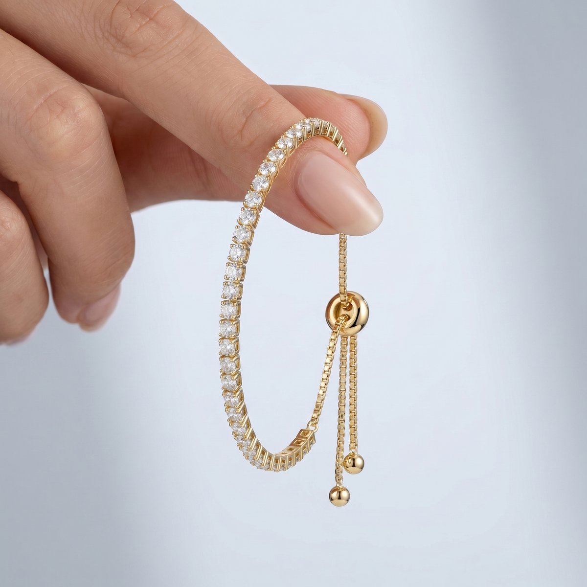 Pulsera tennis ajustable bañada en oro de 18K sostenida entre los dedos, para ver el tamaño real