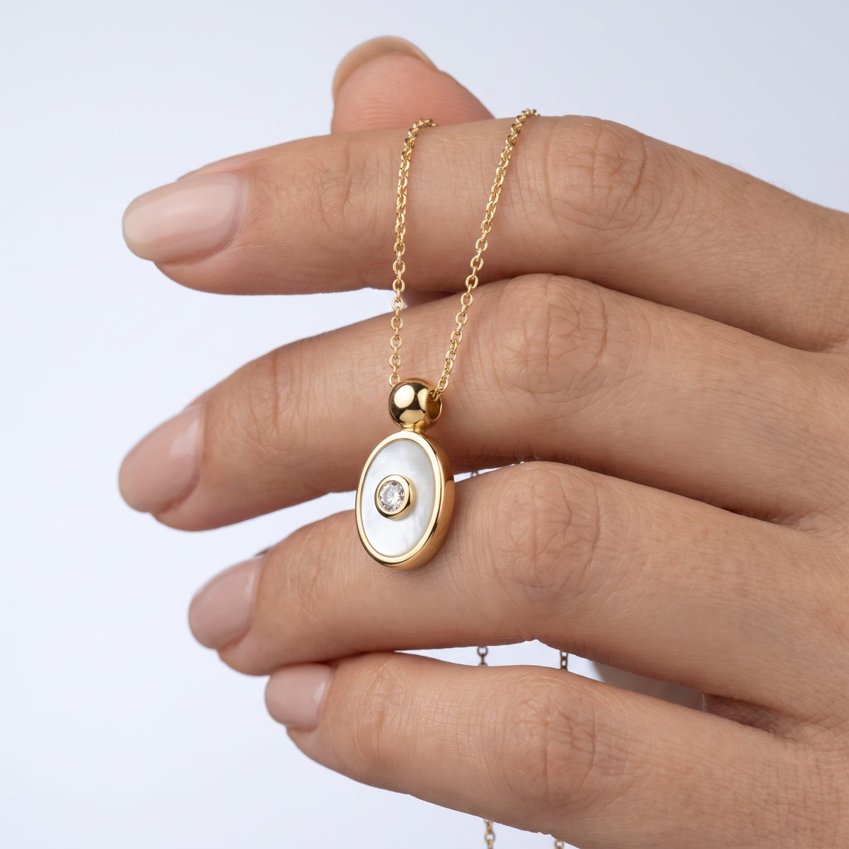 Collar amuleto ojo turco bañado en oro de 18K sostenido entre los dedos, para ver el tamaño real