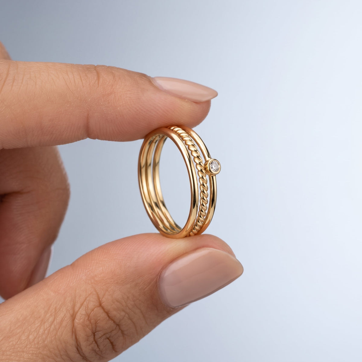 Set de 3 anillos lisos para apilar bañados en oro de 18K sostenidos entre los dedos, para ver el tamaño real