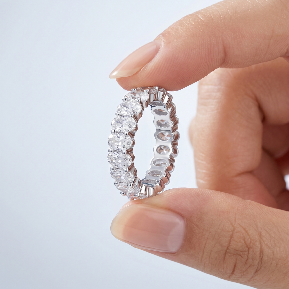 Anillo eternity con circonitas ovaladas color plata sostenido entre los dedos, para ver el tamaño real