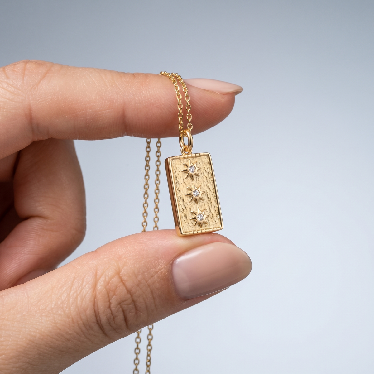 Charm placa con estrellas para collar bañado en oro de 18K sostenido entre los dedos, para ver el tamaño real