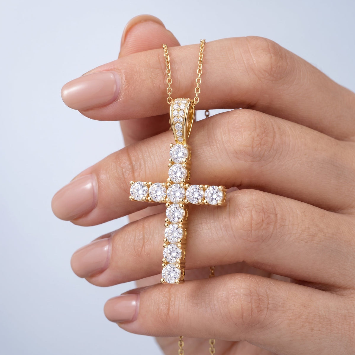 Collar con cruz pequeña bañado en oro de 18K sostenido entre los dedos, para ver el tamaño real