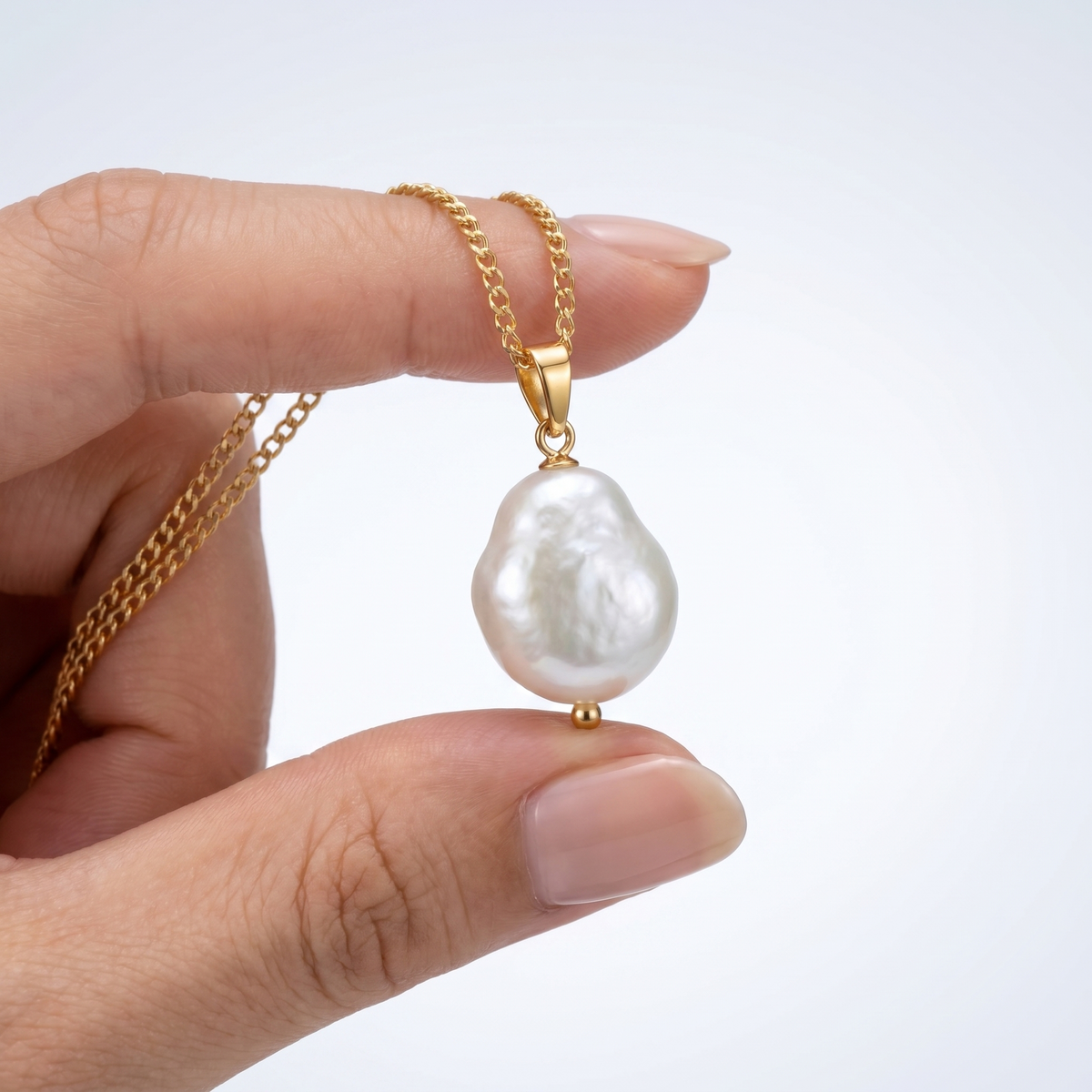 Collar con perla barroca grande bañado en oro de 18K sostenido entre los dedos, para ver el tamaño real