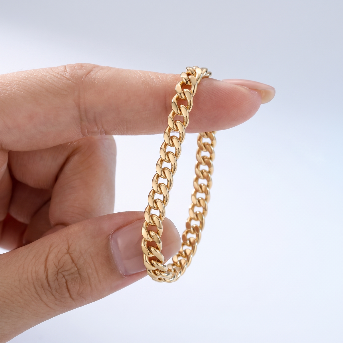 Pulsera de cadena cubana fina bañada en oro de 18K sostenida entre los dedos, para ver el tamaño real