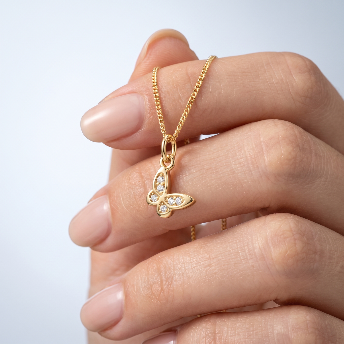 Collar con mariposa bañado en oro de 18K sostenido entre los dedos, para ver el tamaño real