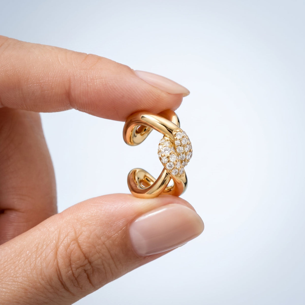 Ear cuff twist sin agujero bañado en oro de 18K sostenido entre los dedos, para ver el tamaño real