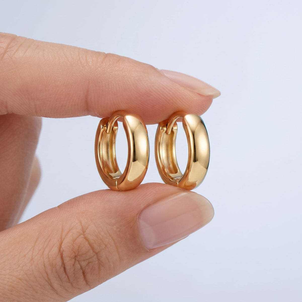 Pendientes huggie lisos bañados en oro de 18K sostenidos entre los dedos, para ver el tamaño real