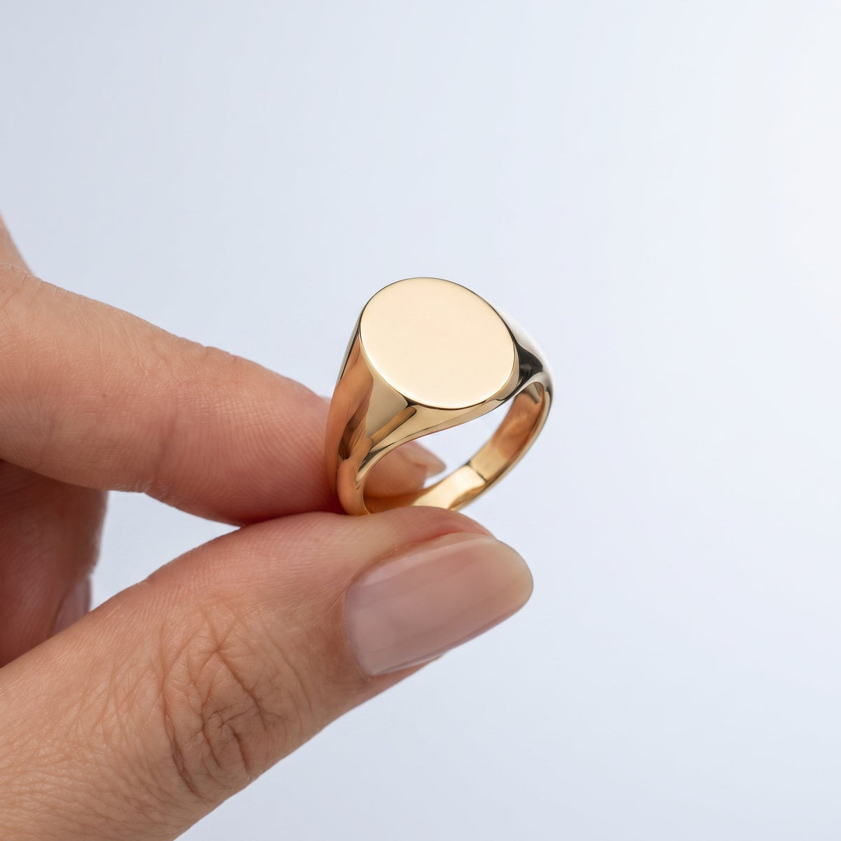 Anillo sello ovalado liso bañado en oro de 18K sostenido entre los dedos, para ver el tamaño real