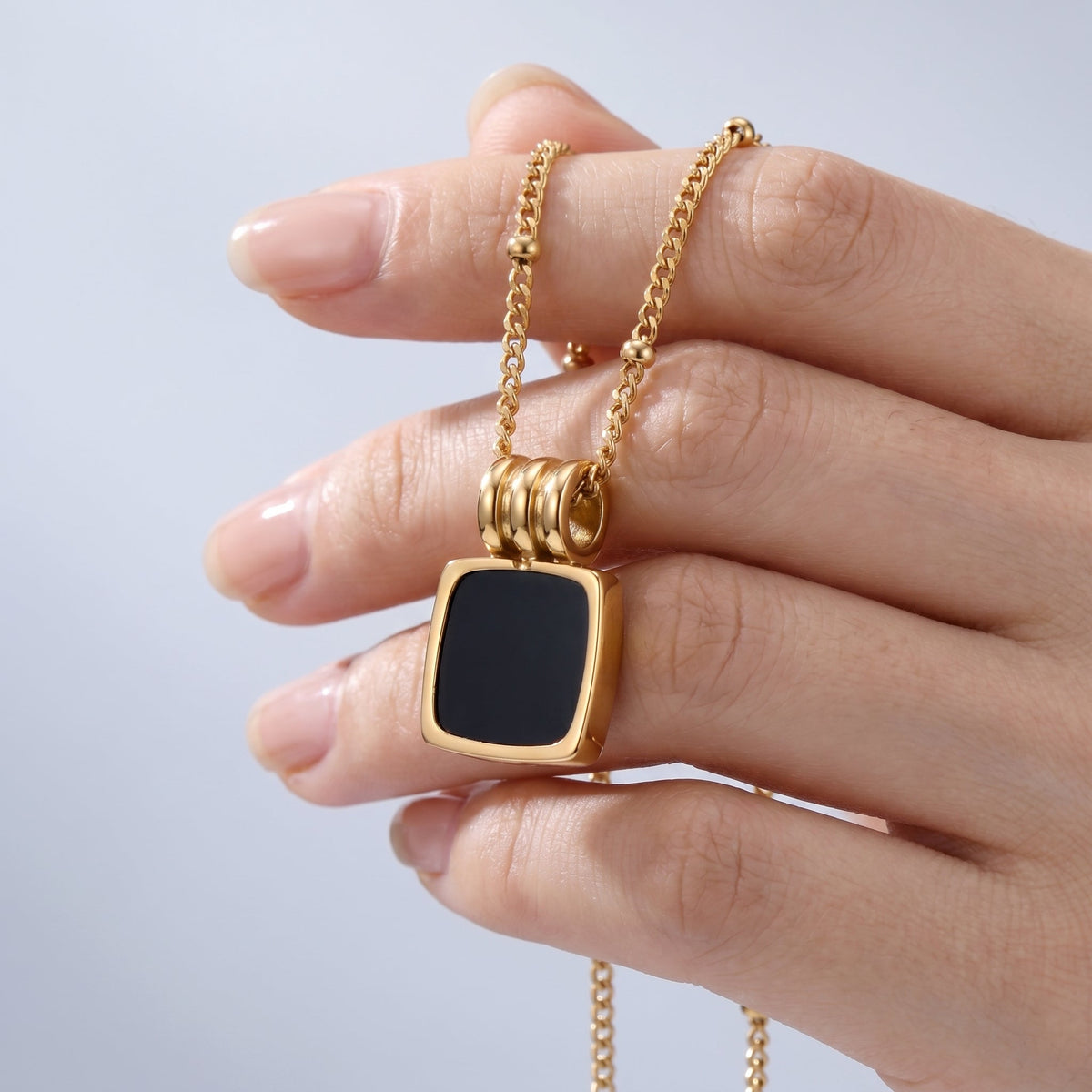 Collar con colgante de concha negra bañado en oro de 18K sostenido entre los dedos, para ver el tamaño real