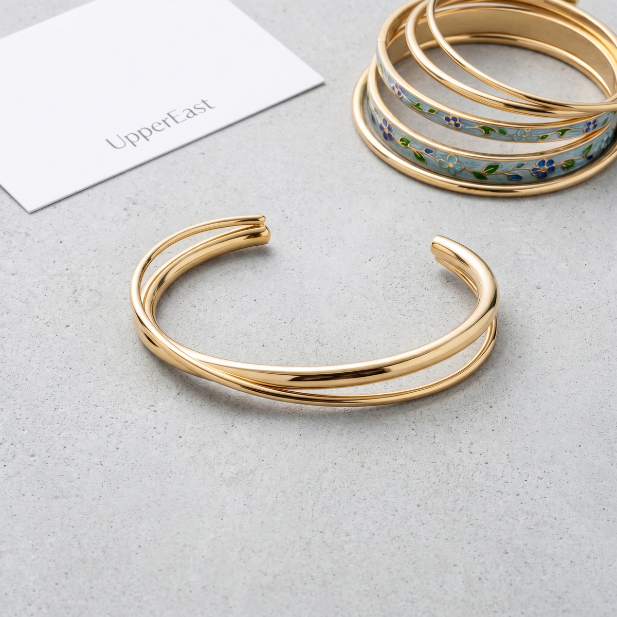 Brazalete rígido cruzado bañado en oro de 18K combinado con otras joyas UpperEast