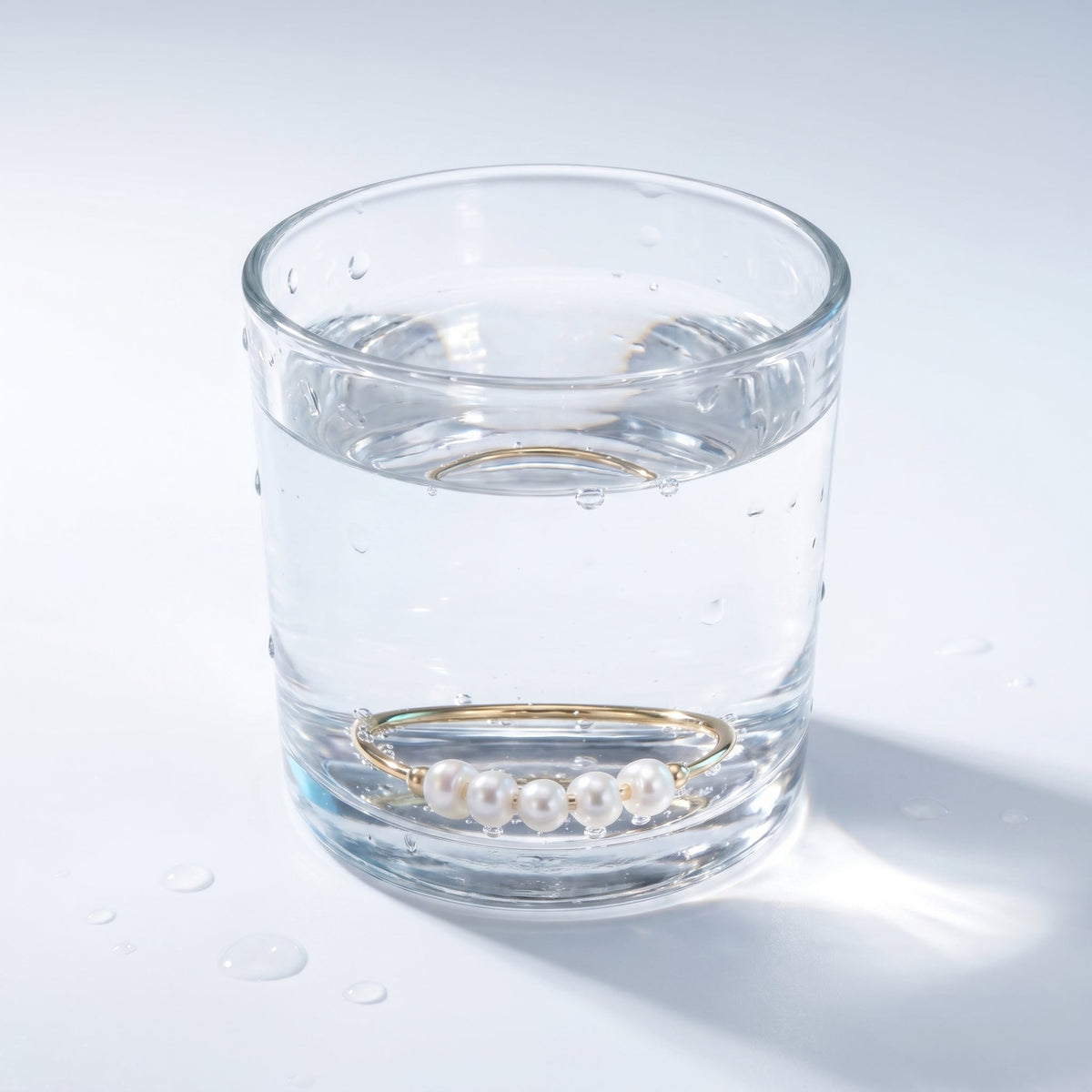 Anillo fino con 5 perlitas bañado en oro de 18K en un vaso de agua