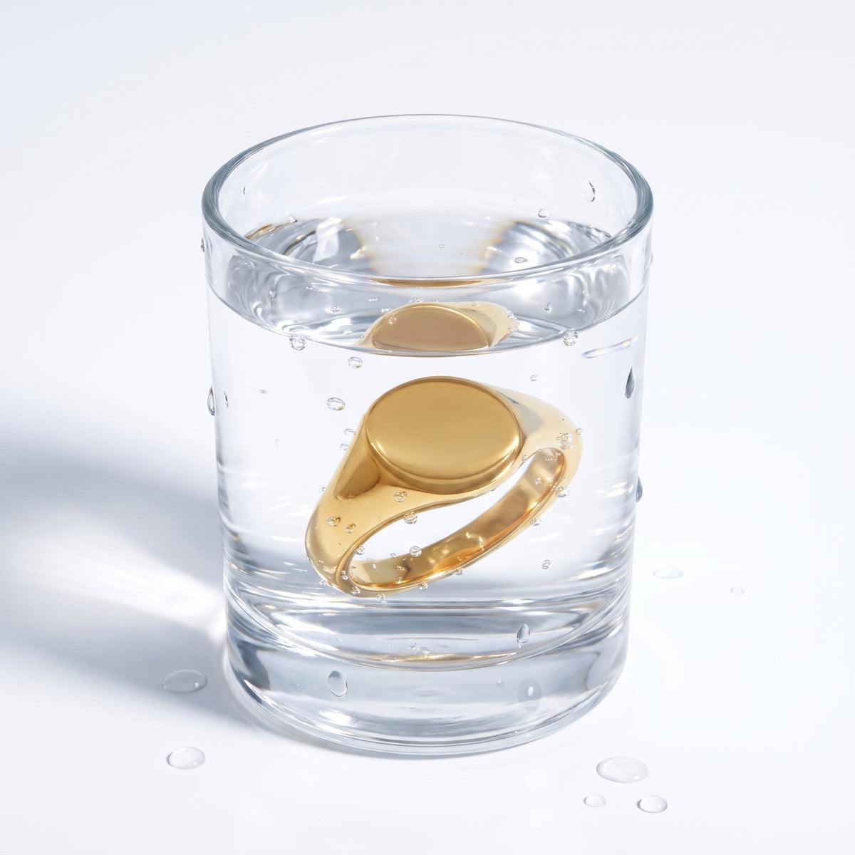 Anillo sello ovalado liso bañado en oro de 18K en un vaso de agua