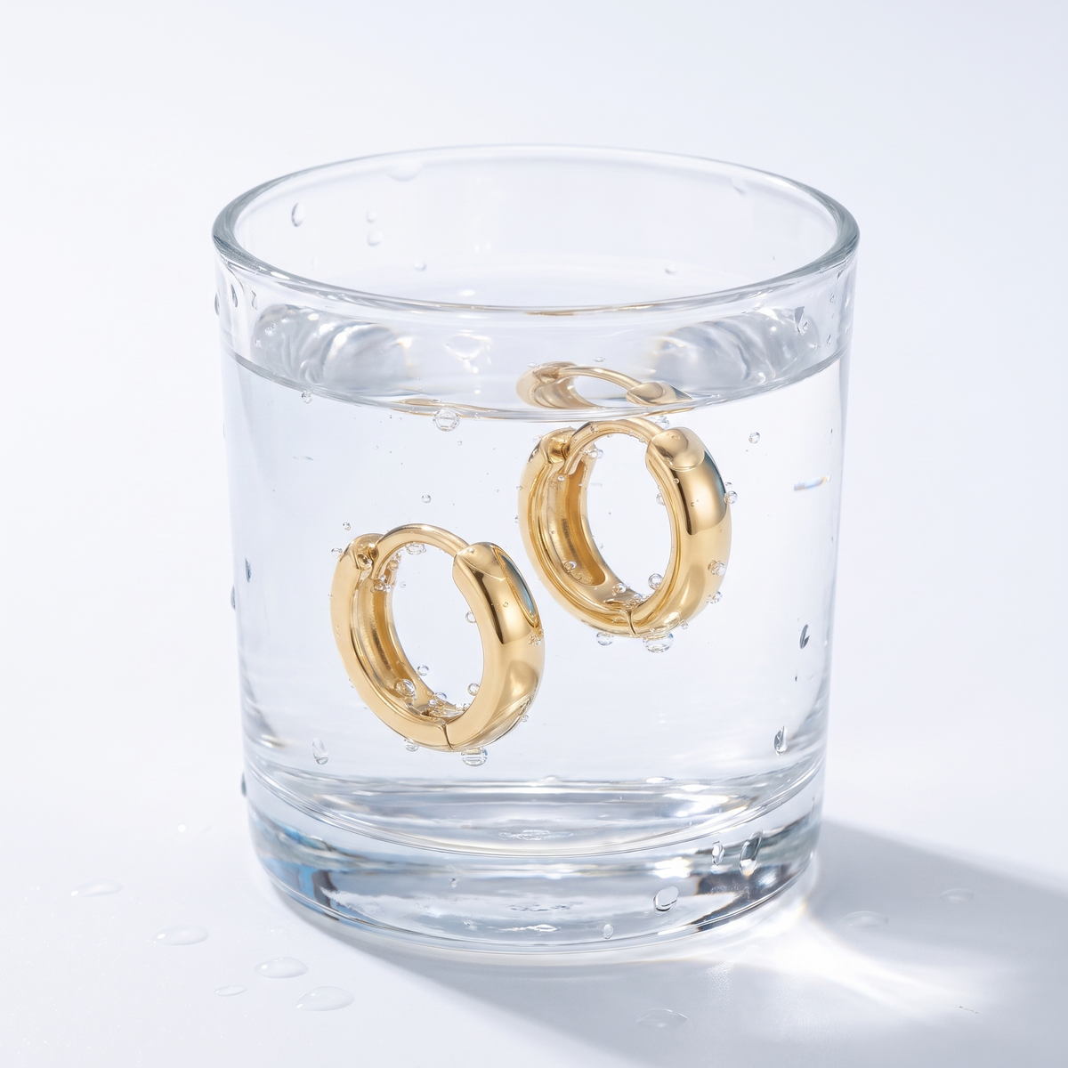 Pendientes huggie lisos bañados en oro de 18K en un vaso de agua
