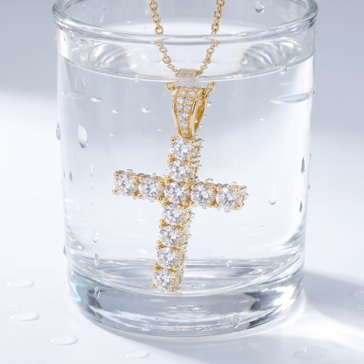 Collar con cruz pequeña bañado en oro de 18K en un vaso de agua