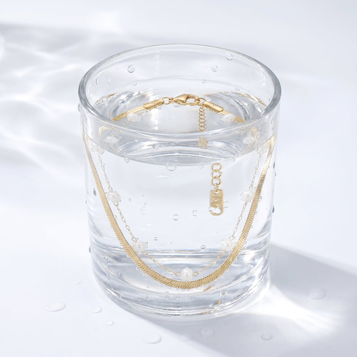 Tobillera doble de cadena snake bañada en oro de 18K en un vaso de agua