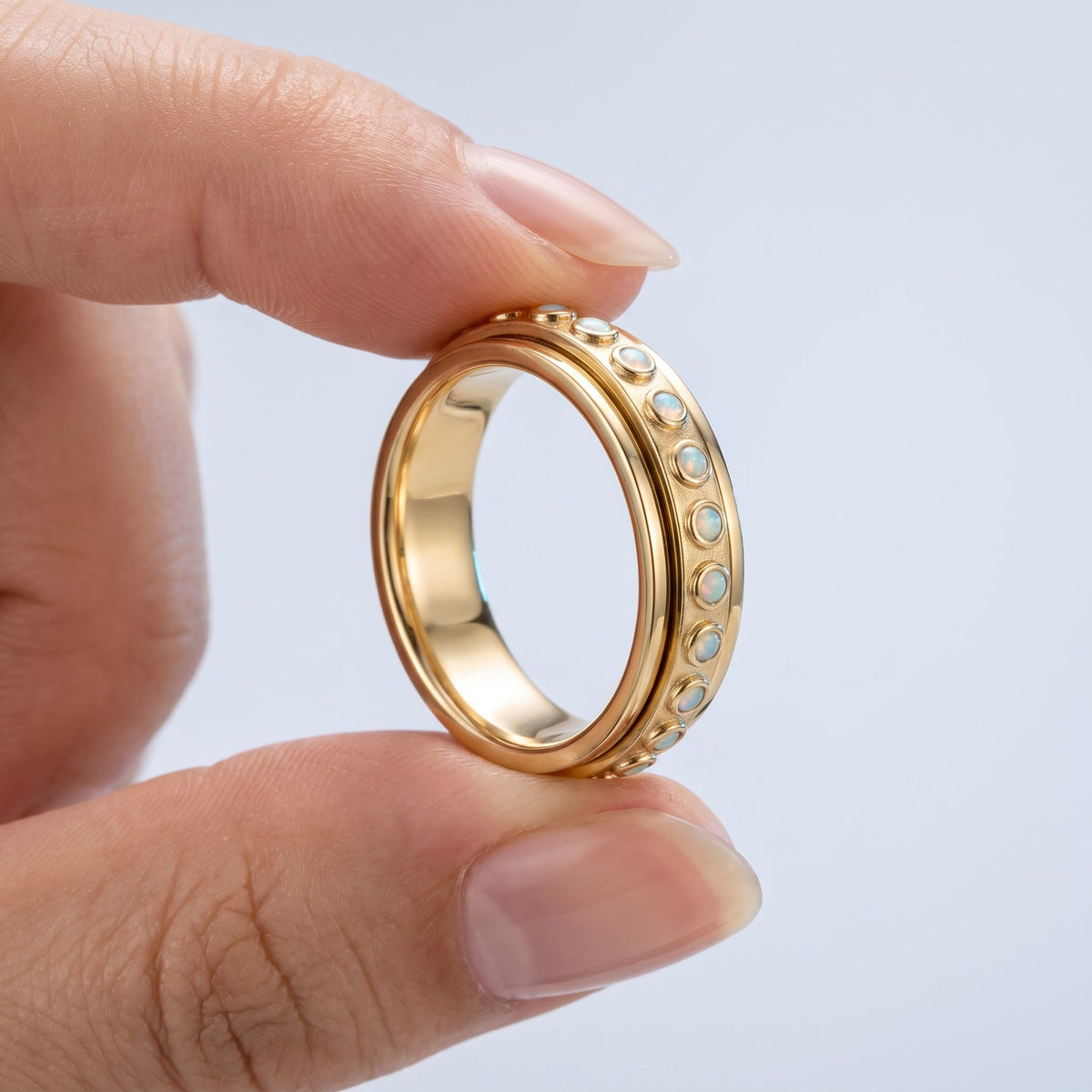 Anillo antiestrés giratorio bañado en oro de 18K sostenido entre los dedos, para ver el tamaño real