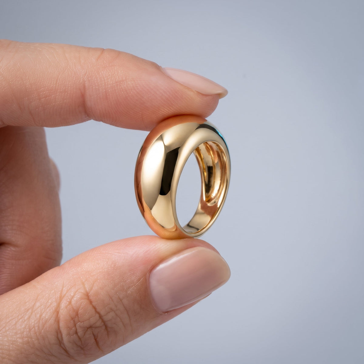 Anello bombato a cupola liscio placcato oro 18K tenuto tra le dita, per vedere le dimensioni reali