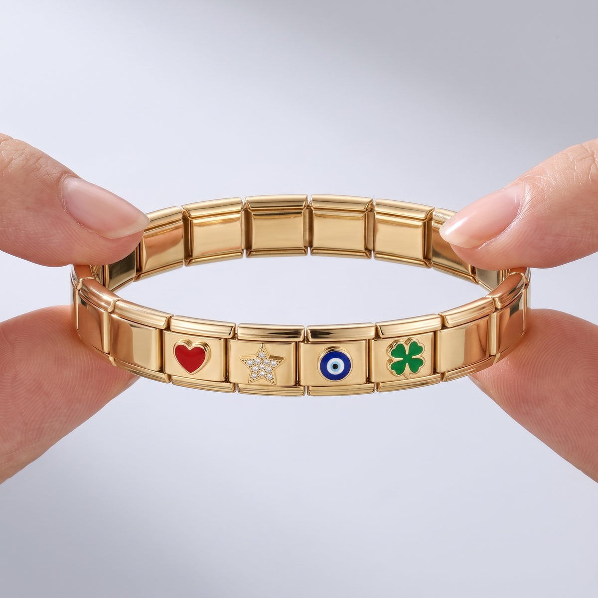 Pulsera modular con charms bañada en oro de 18K sostenida entre los dedos, para ver el tamaño real
