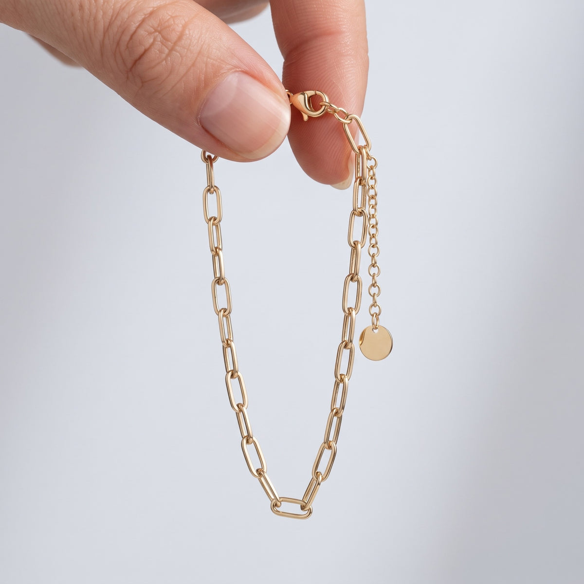 Pulsera de cadena paperclip bañada en oro de 18K sostenida entre los dedos, para ver el tamaño real