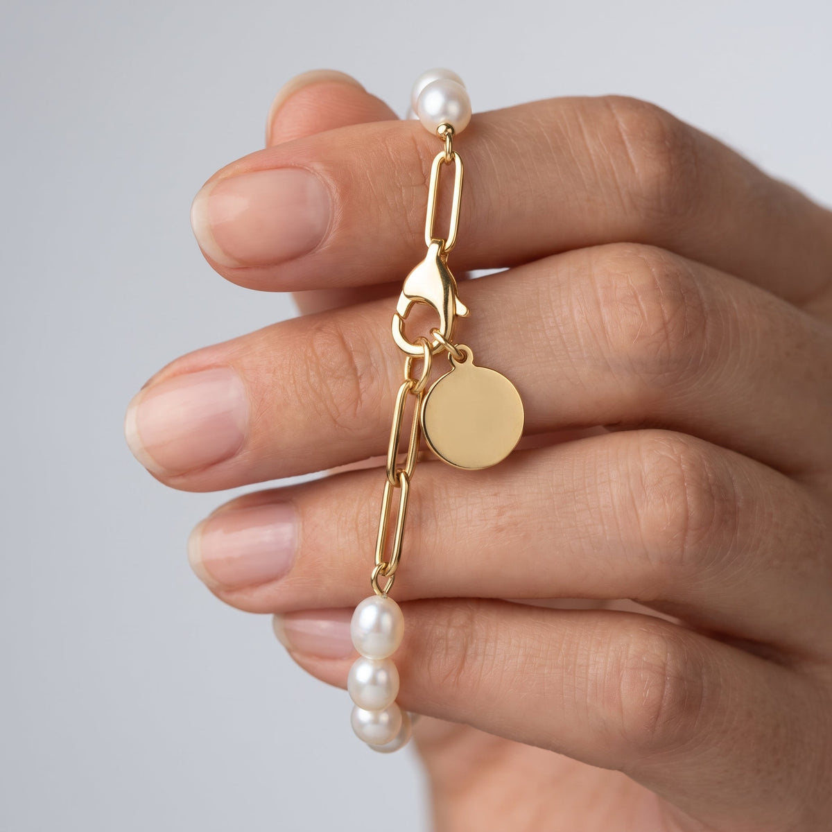 Pulsera de perlas y paperclip bañada en oro de 18K sostenida entre los dedos, para ver el tamaño real