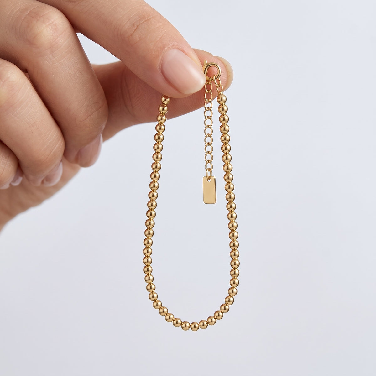 Bracciale a palline placcato oro 18K tenuto tra le dita, per vedere le dimensioni reali