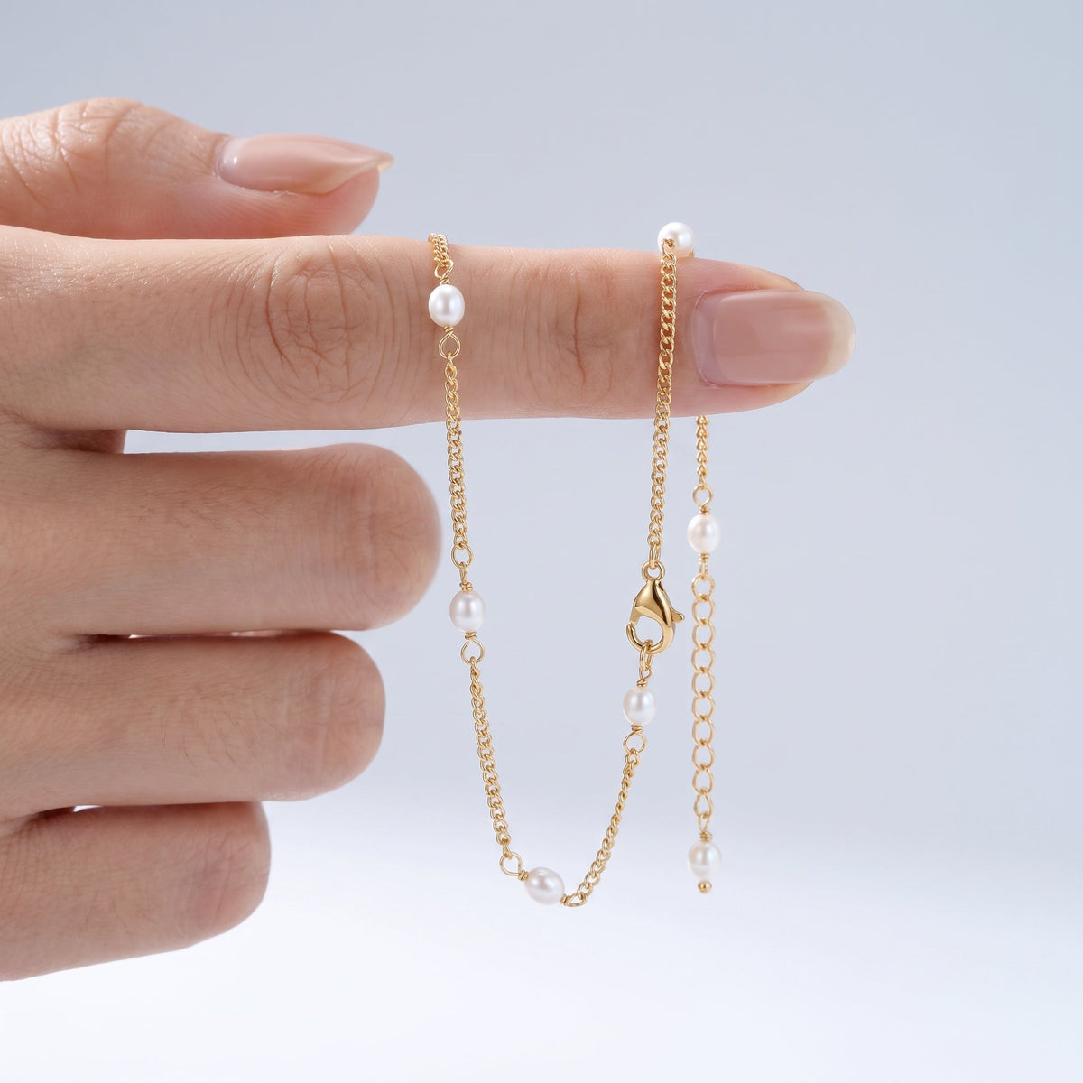 Tobillera con perlitas bañada en oro de 18K sostenida entre los dedos, para ver el tamaño real