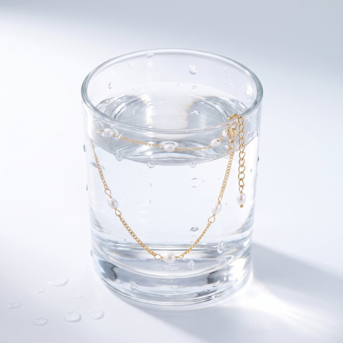 Tobillera con perlitas bañada en oro de 18K en un vaso de agua