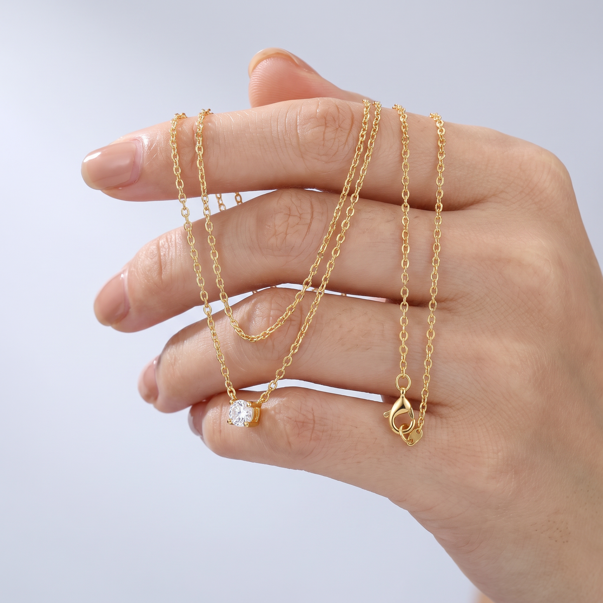 Collar en capas con punto de luz bañado en oro de 18K sostenido entre los dedos, para ver el tamaño real