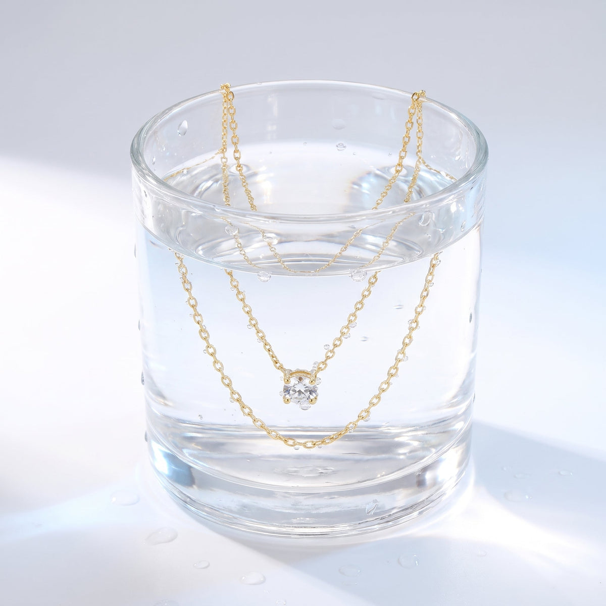 Collar en capas con punto de luz bañado en oro de 18K en un vaso de agua
