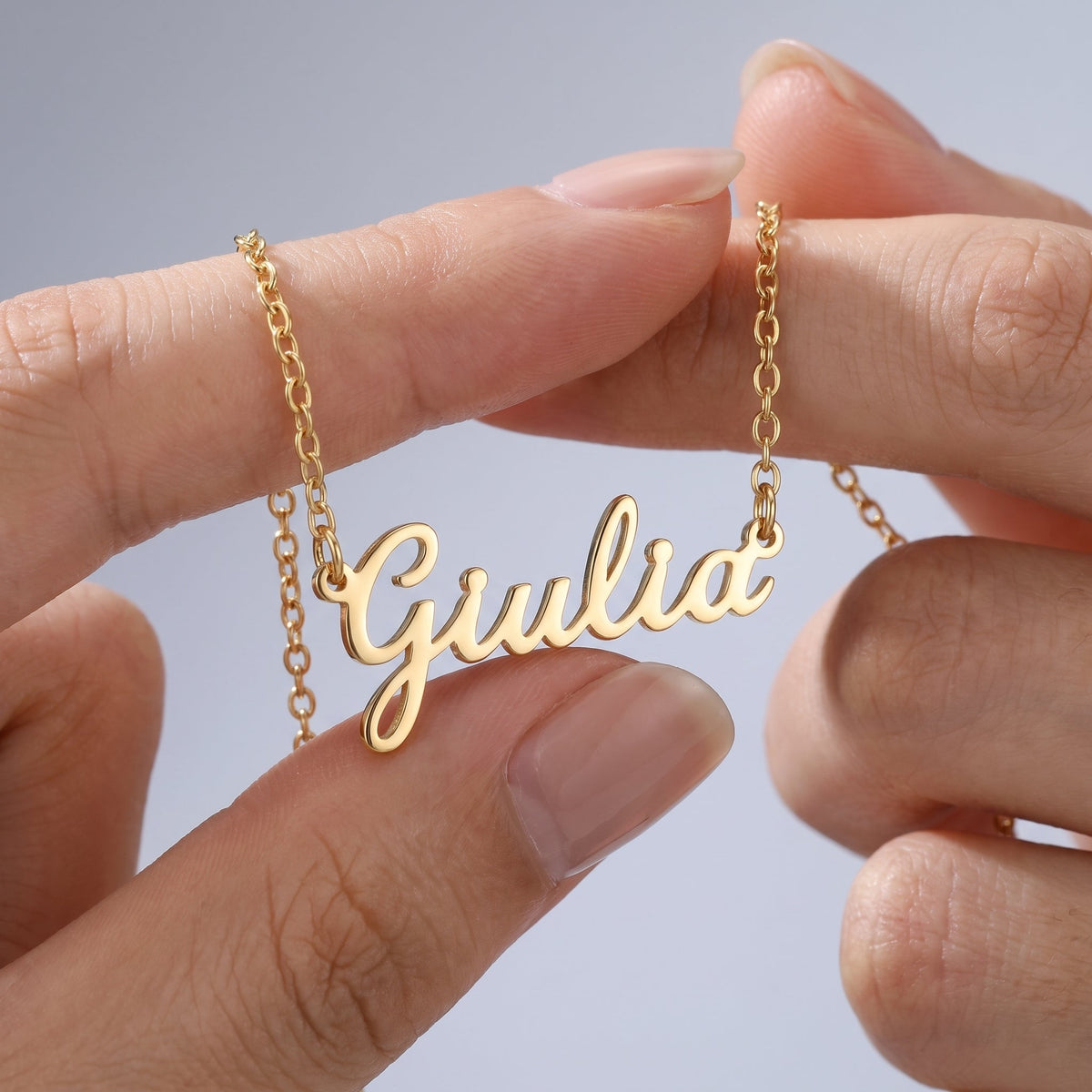 Collar con nombre en cursiva bañado en oro de 18K sostenido entre los dedos, para ver el tamaño real