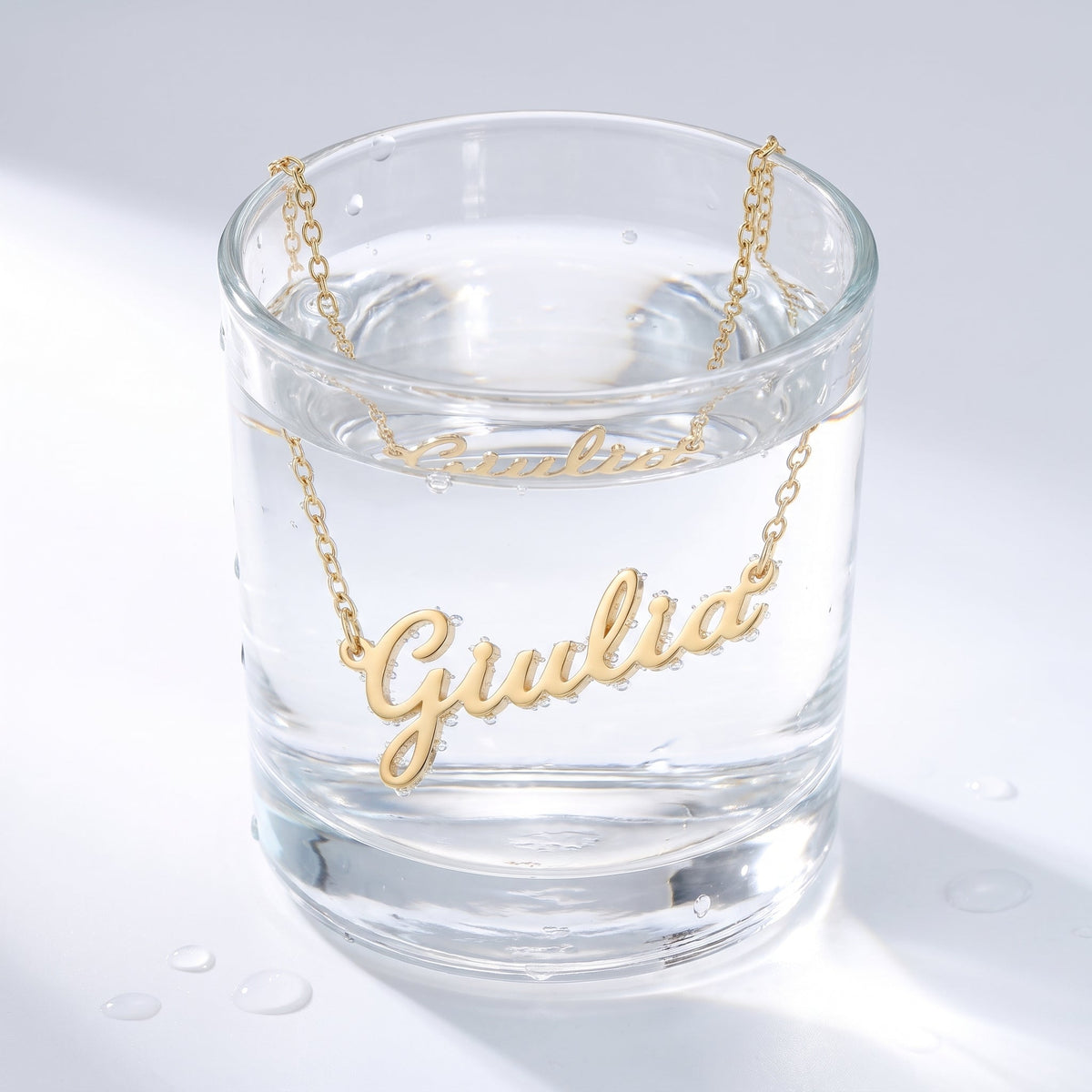 Collar con nombre en cursiva bañado en oro de 18K en un vaso de agua