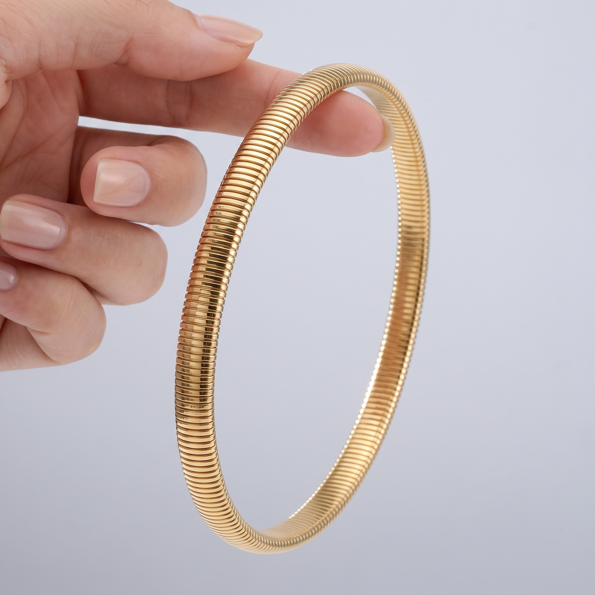 Gargantilla tubogas bañada en oro de 18K sostenida entre los dedos, para ver el tamaño real