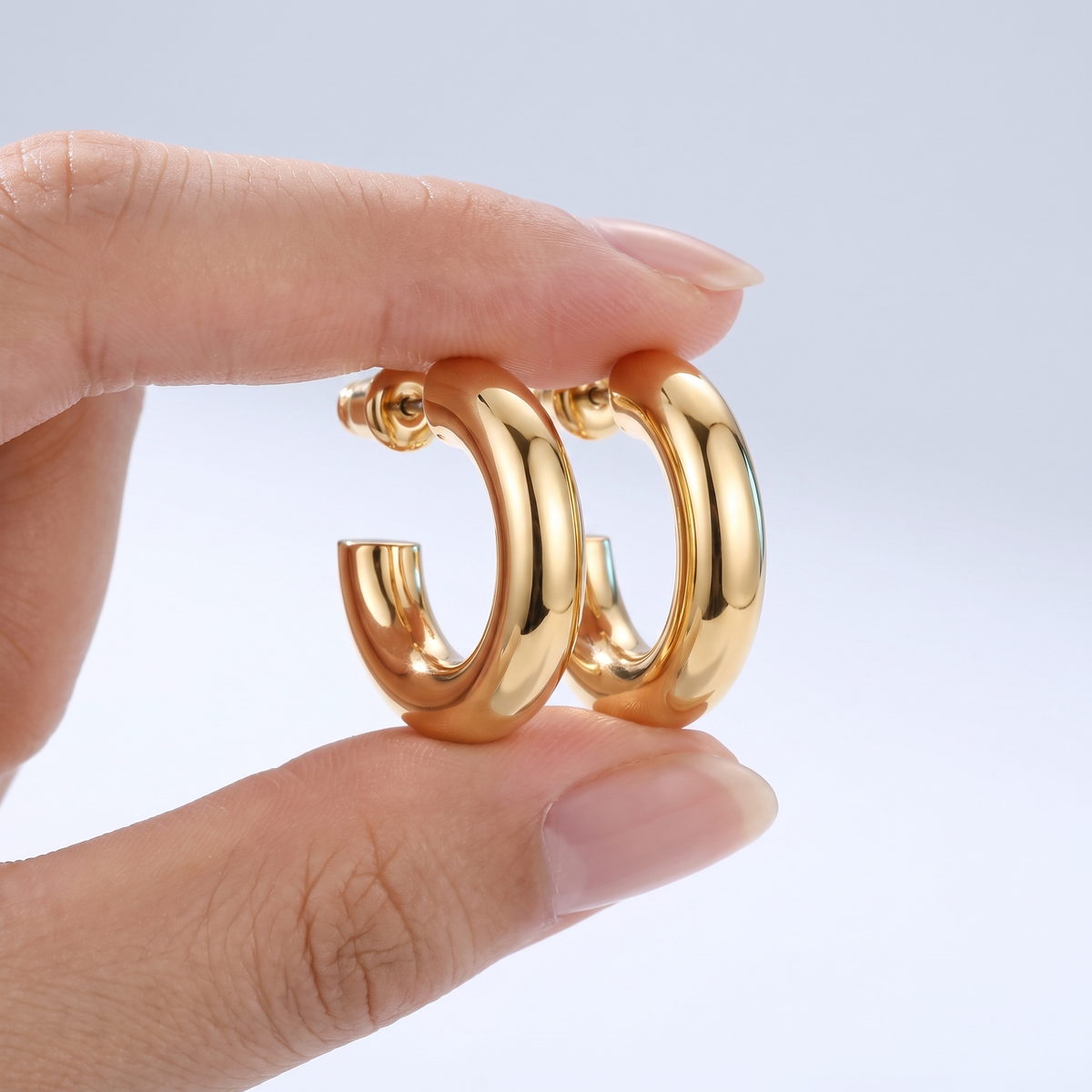 Pendientes de aro gruesos chunky bañados en oro de 18K sostenidos entre los dedos, para ver el tamaño real