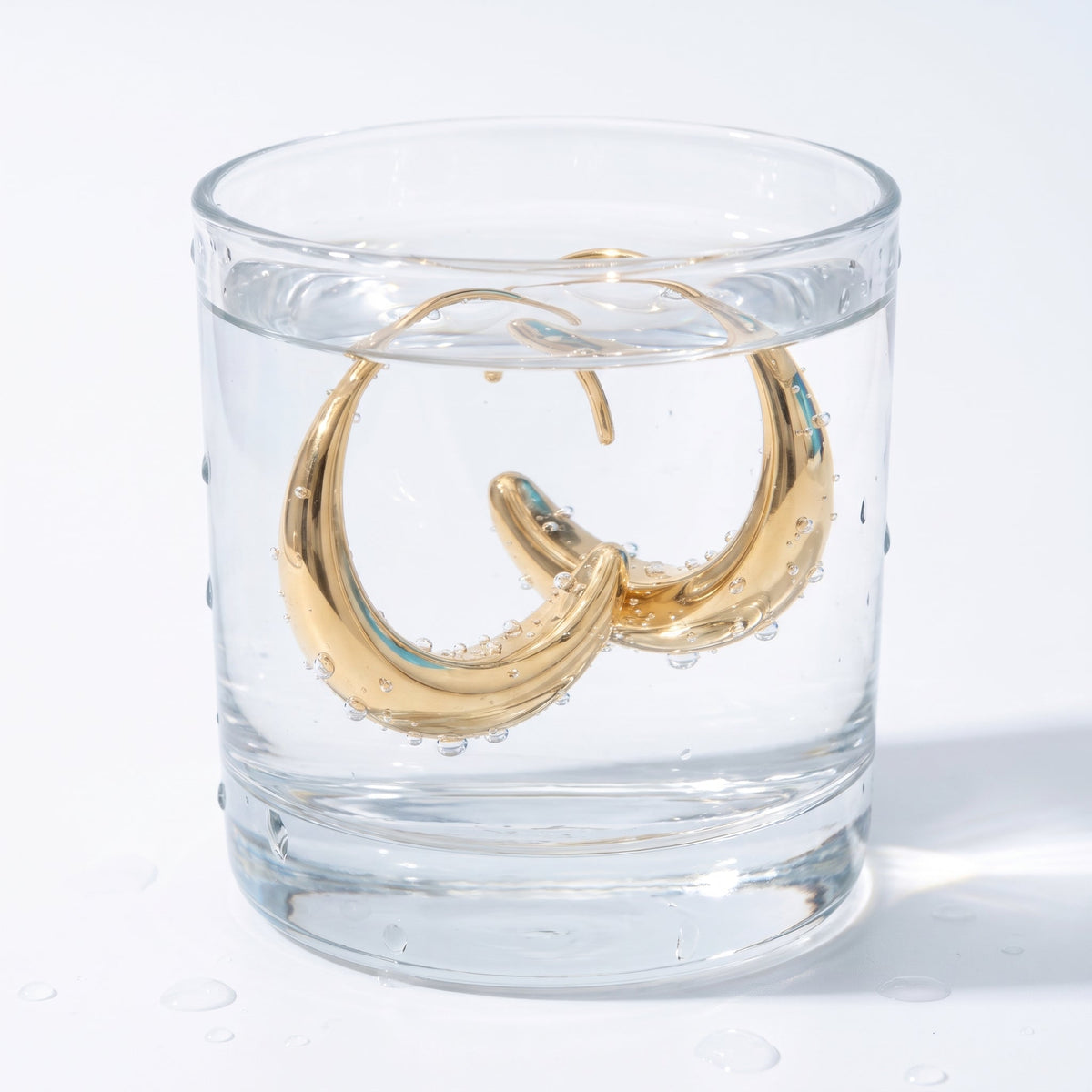Pendientes ovalados pasantes bañados en oro de 18K en un vaso de agua