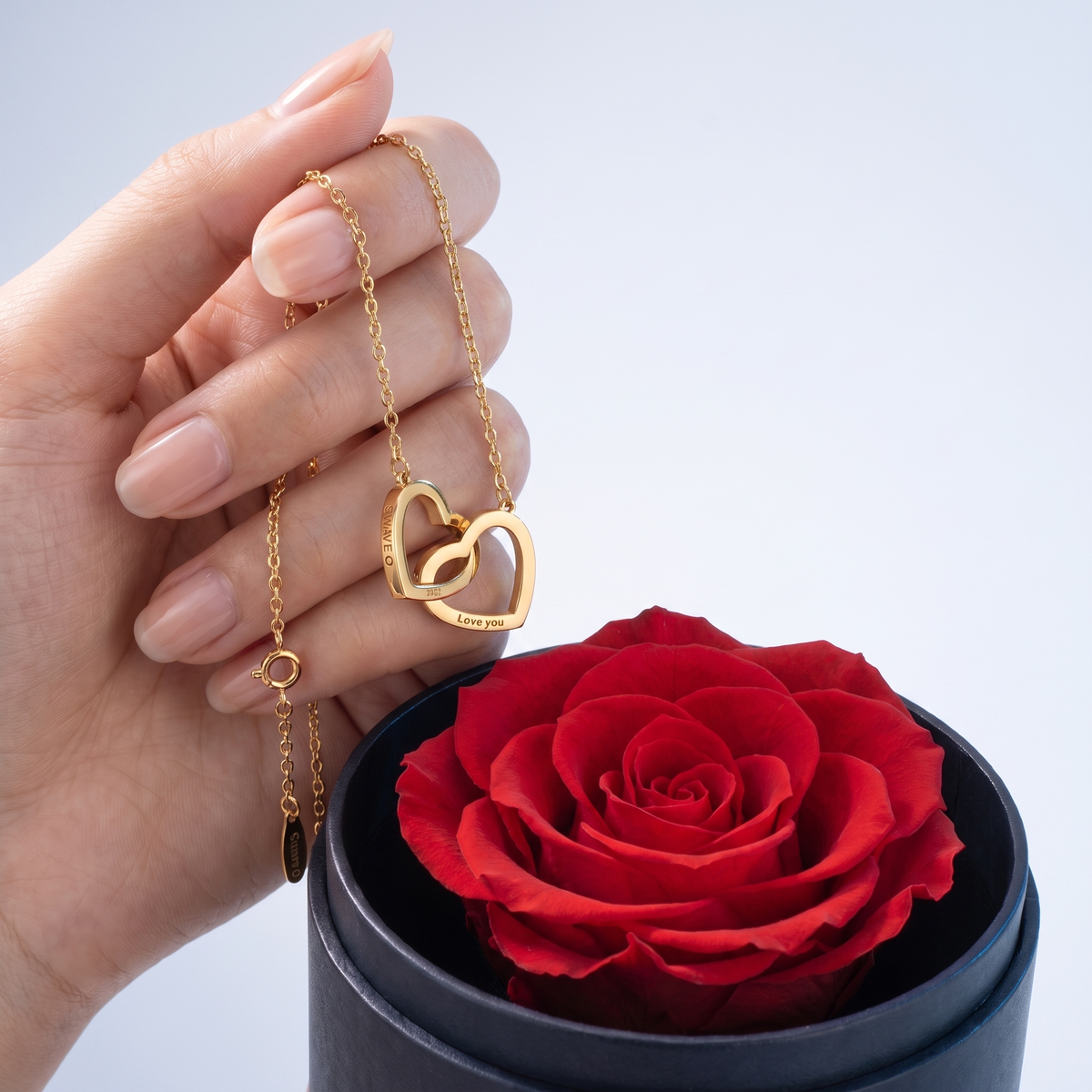 Set regalo de rosa preservada y collar de corazones sostenido entre los dedos, para ver el tamaño real