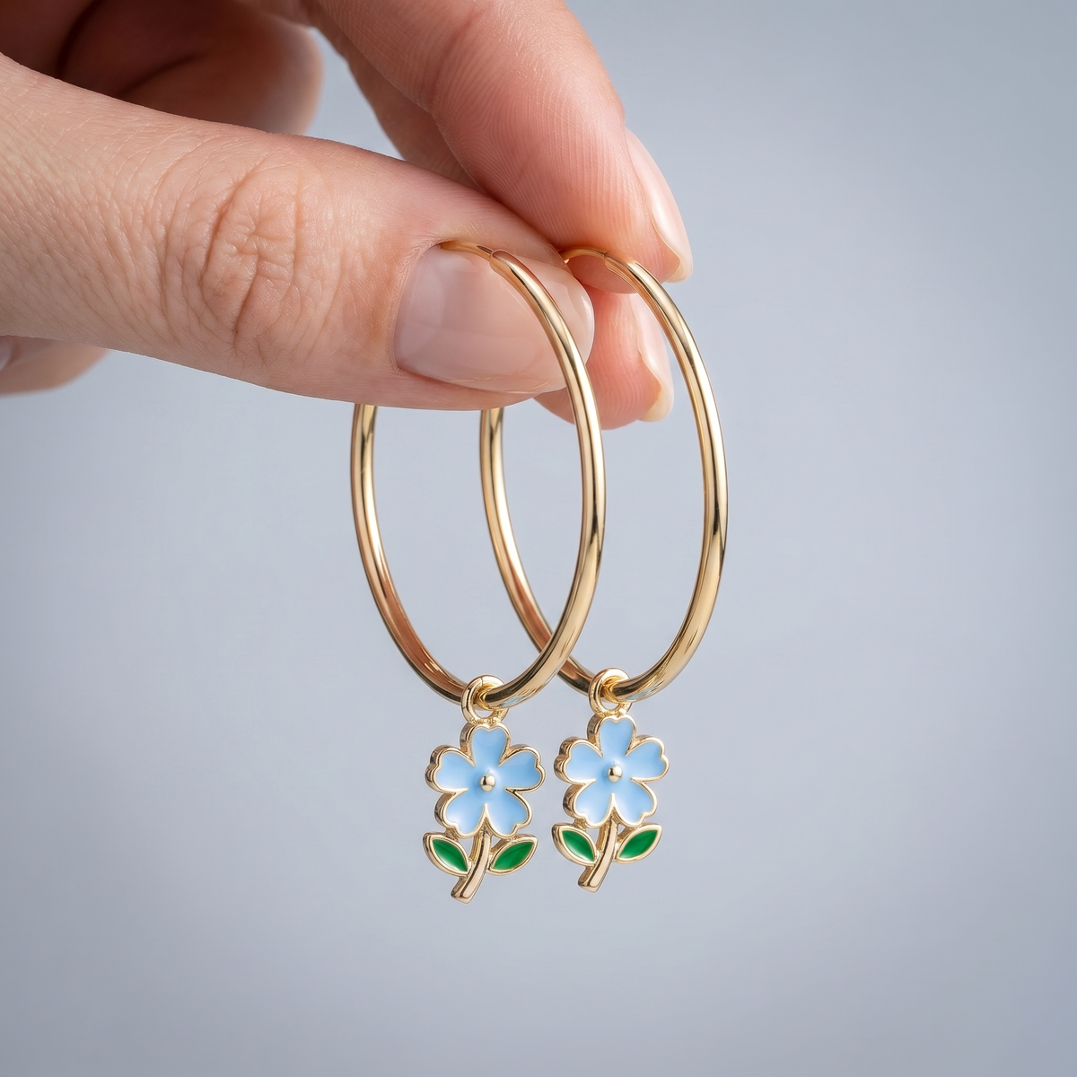 Pendientes de aro maxi con flores bañados en oro de 18K sostenidos entre los dedos, para ver el tamaño real
