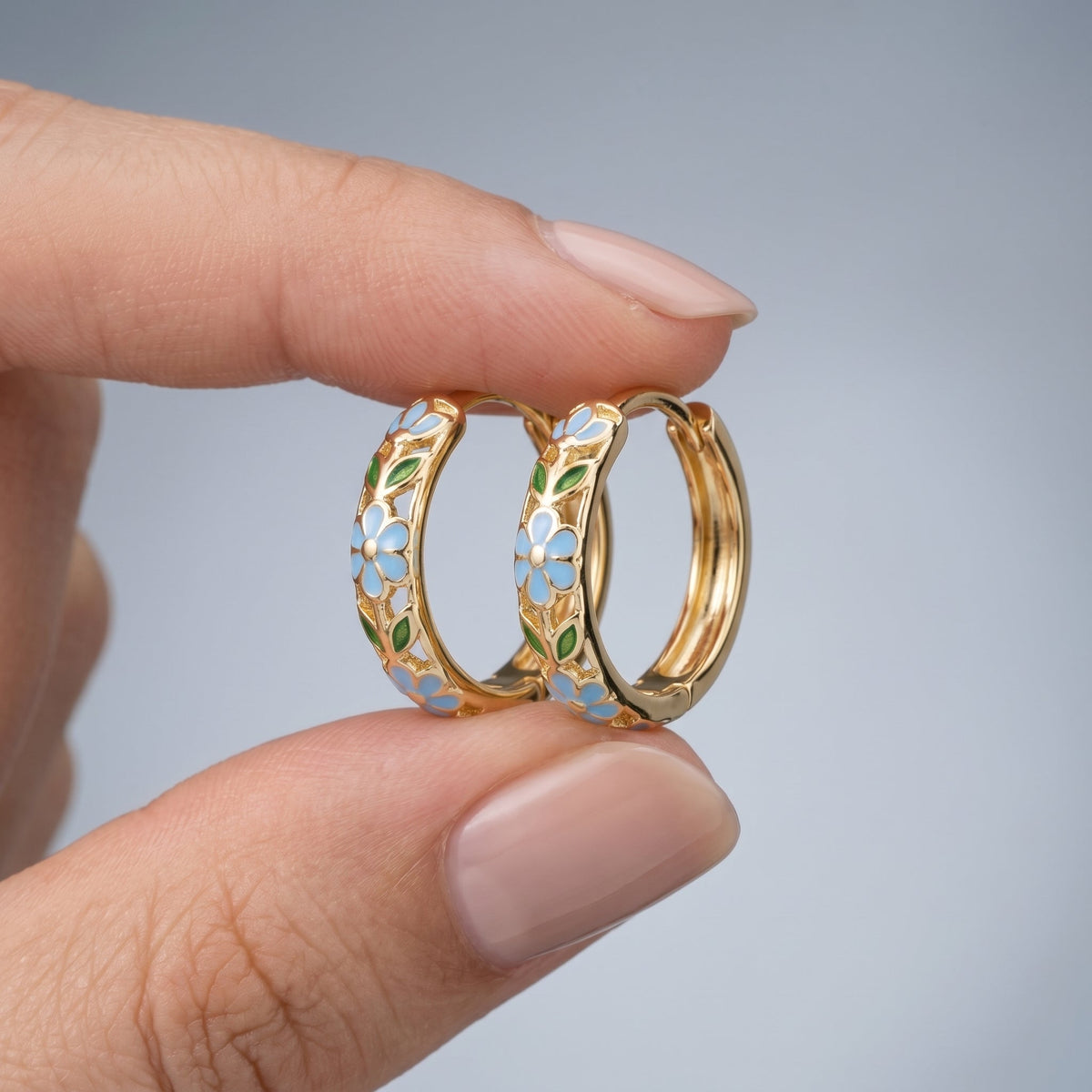 Pendientes de aro con flores bañados en oro de 18K sostenidos entre los dedos, para ver el tamaño real