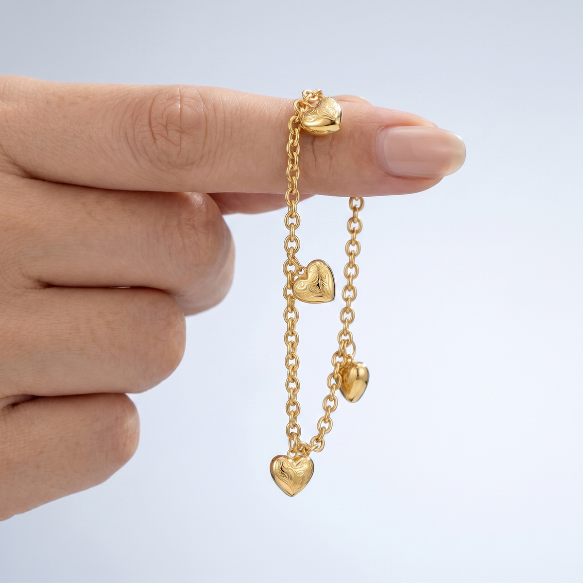 Pulsera con charms de corazones bañada en oro de 18K sostenida entre los dedos, para ver el tamaño real