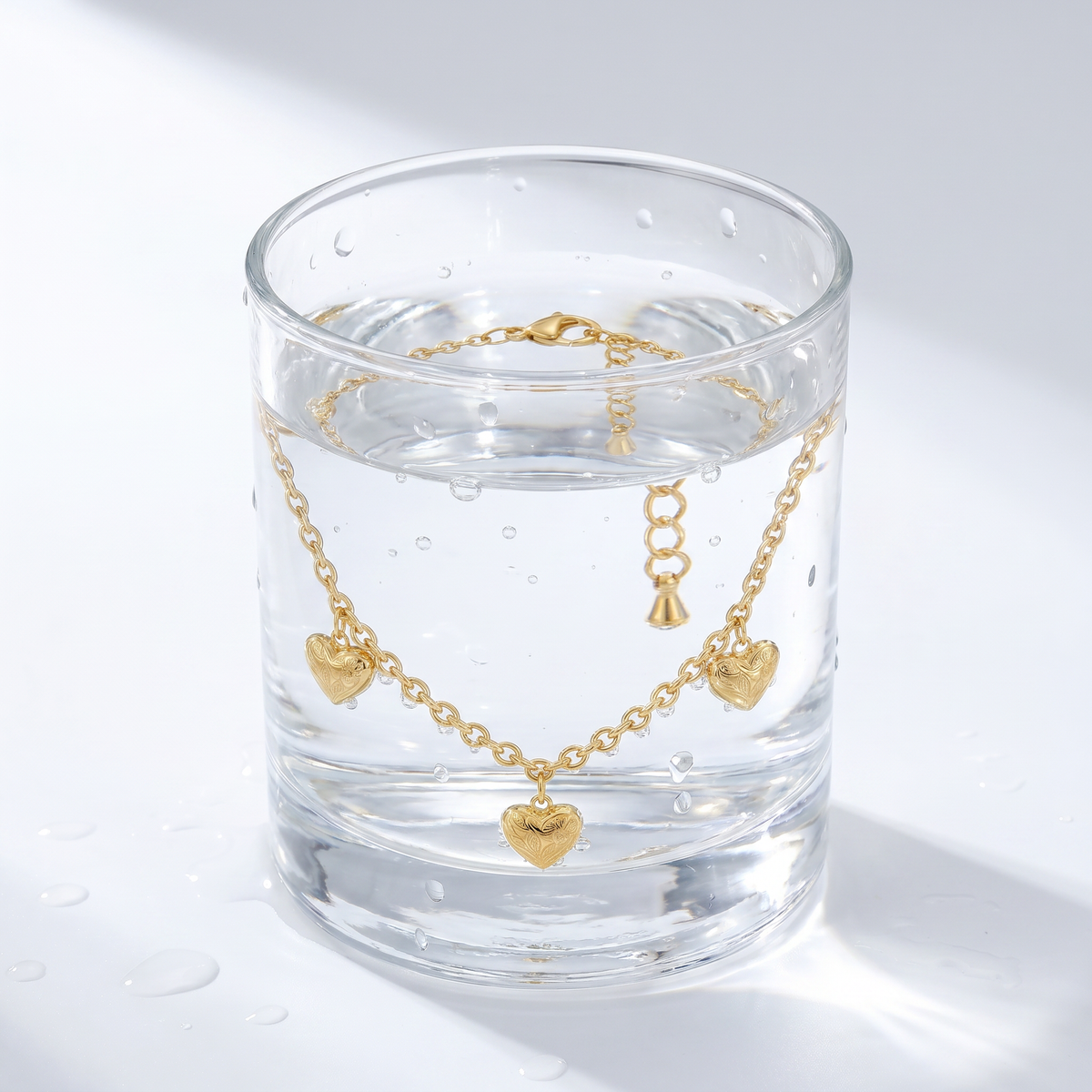 Pulsera con charm de corazón bañada en oro de 18K en un vaso de agua