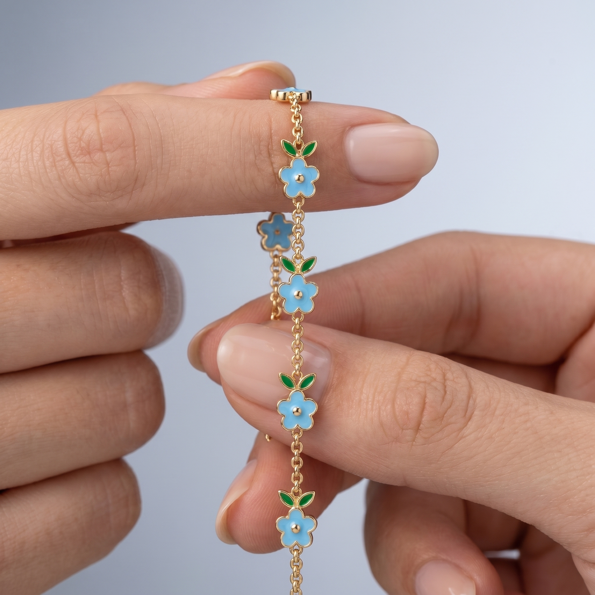 Pulsera con flores esmaltadas bañada en oro de 18K sostenida entre los dedos, para ver el tamaño real
