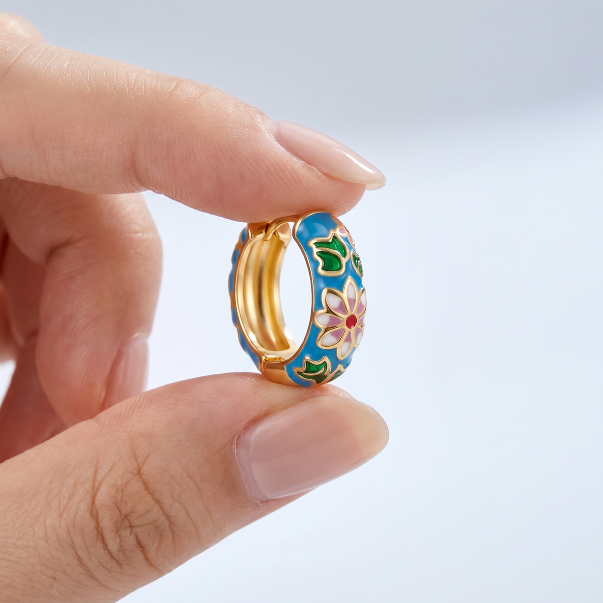 Pendientes flor cloisonné bañados en oro de 18K sostenidos entre los dedos, para ver el tamaño real