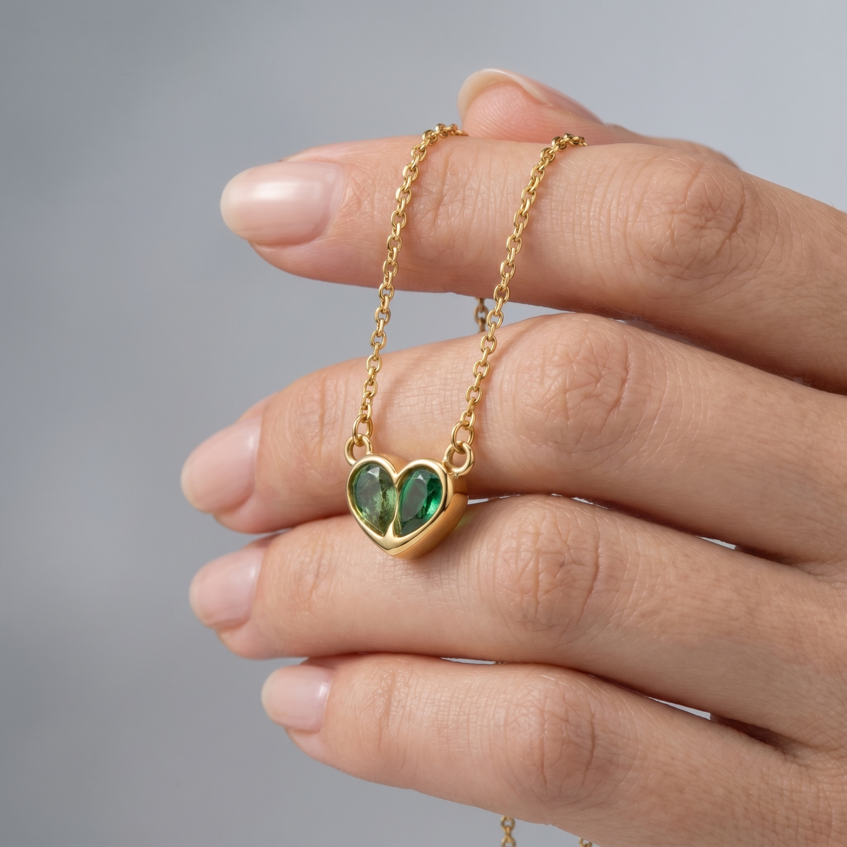 Collar corazón verde esmeralda bañado en oro de 18K sostenido entre los dedos, para ver el tamaño real