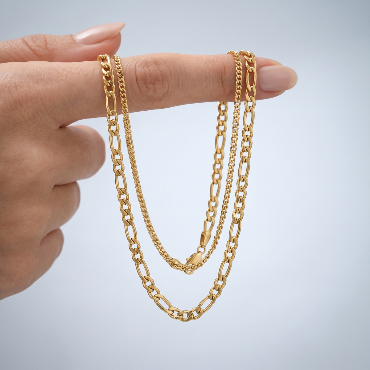 Collar doble figaro en capas bañado en oro de 18K sostenido entre los dedos, para ver el tamaño real