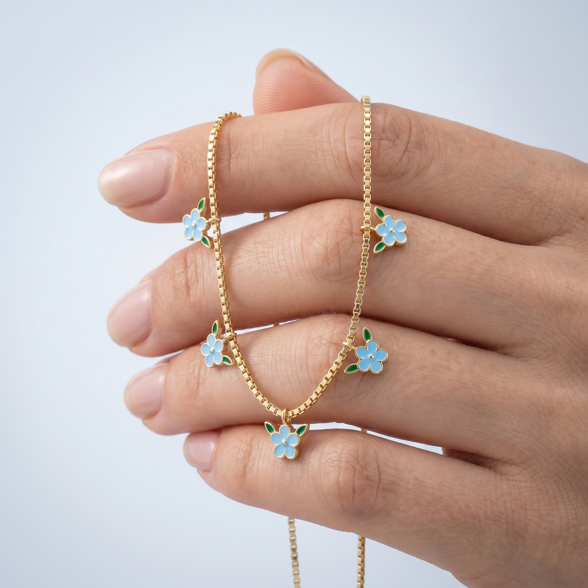 Collana con fiori smaltati azzurri placcata oro 18K tenuta tra le dita, per vedere le dimensioni reali